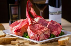 Raw steaks presented on a plate, ready to cook, with a bottle of wine