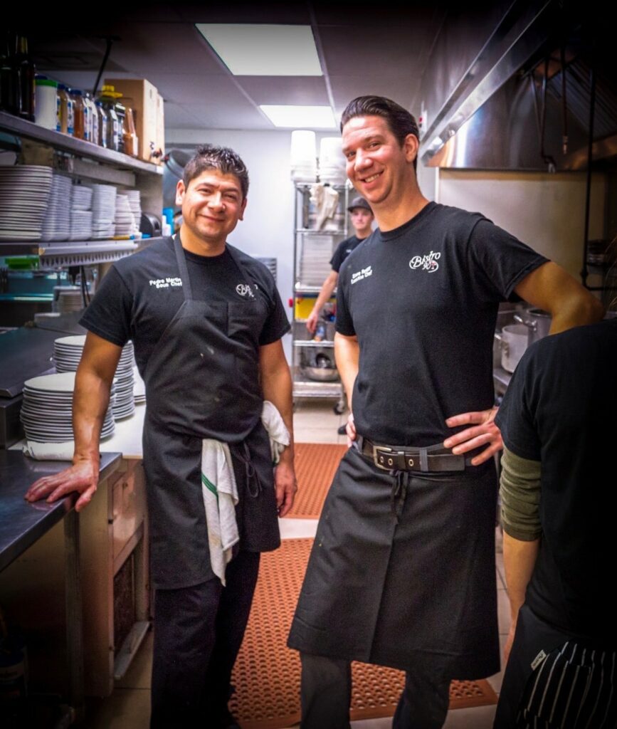 Two chefs standing smiling in a restaurant kitchen